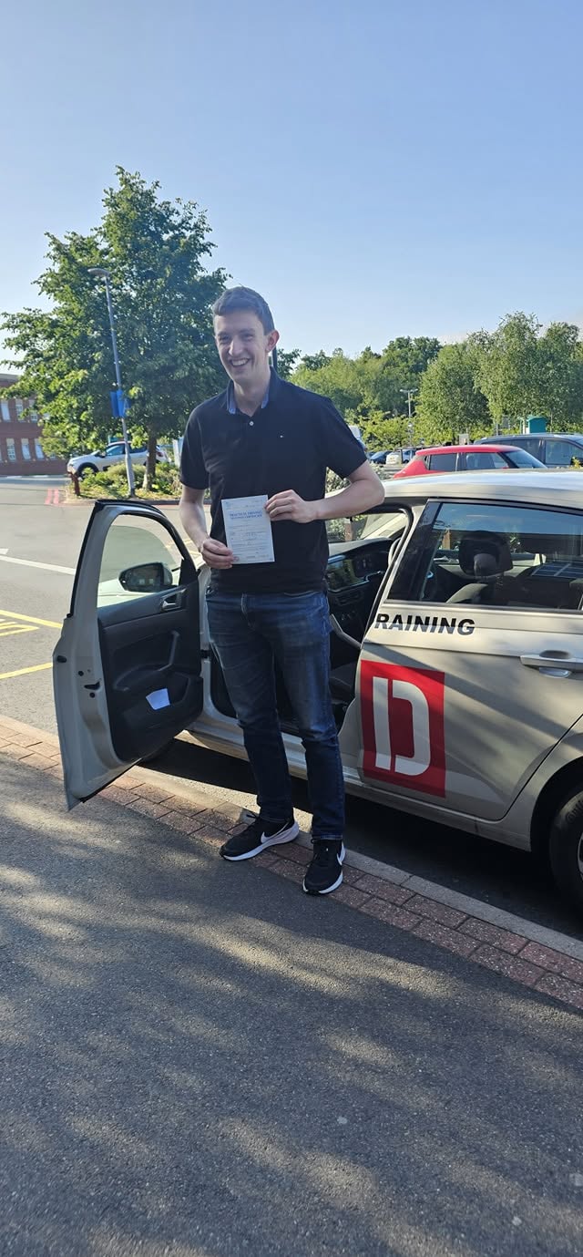 A learner standing beside the driving school car on a bright sunny day, smiling and holding their practical driving test pass certificate