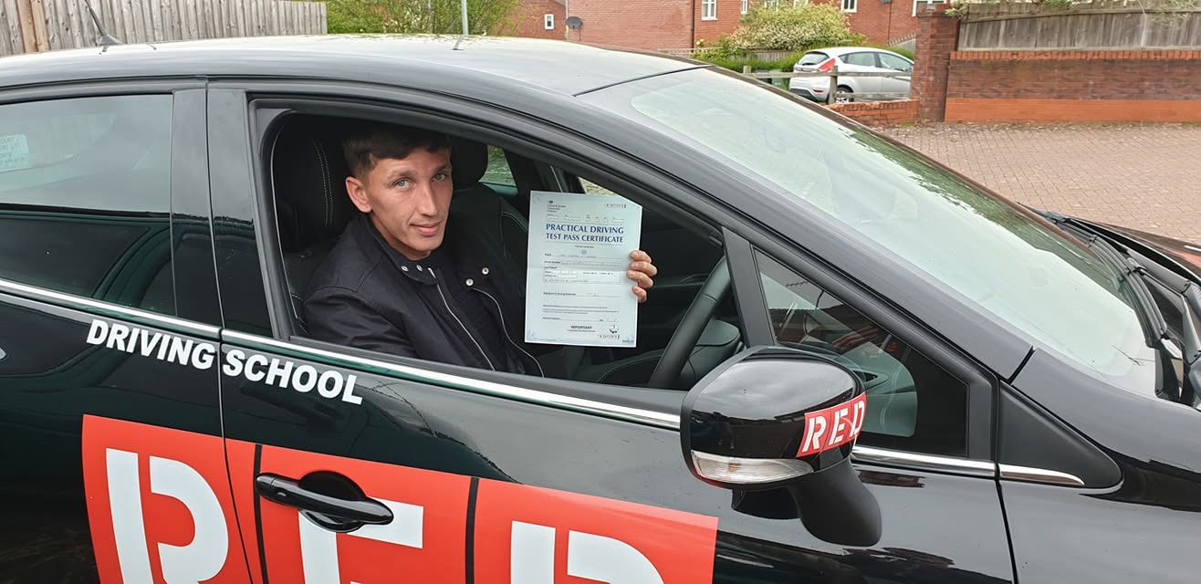 A learner holding a practical driving test pass certificate in the driving school car