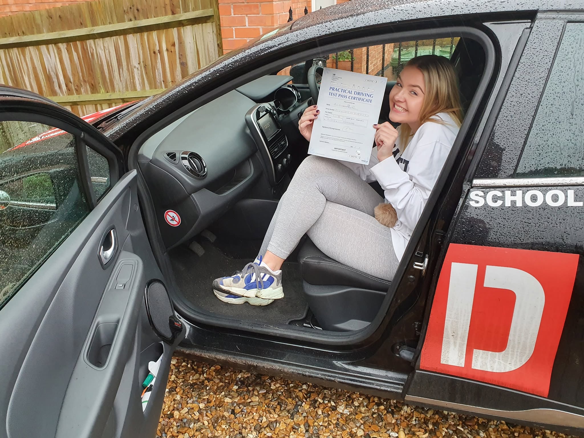 A learner giving a thumbs up while holding their practical driving test pass certificate